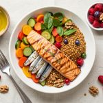 Vue du dessus d’une table lumineuse présentant du saumon, des sardines, des légumes colorés, des lentilles, des noix, de l’huile d’olive et des fruits rouges.